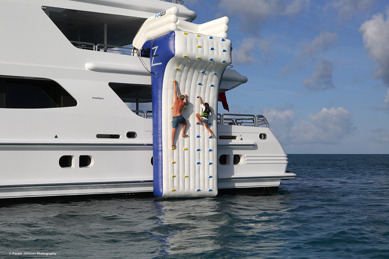 couple climbing up inflatable wall on side of superyacht